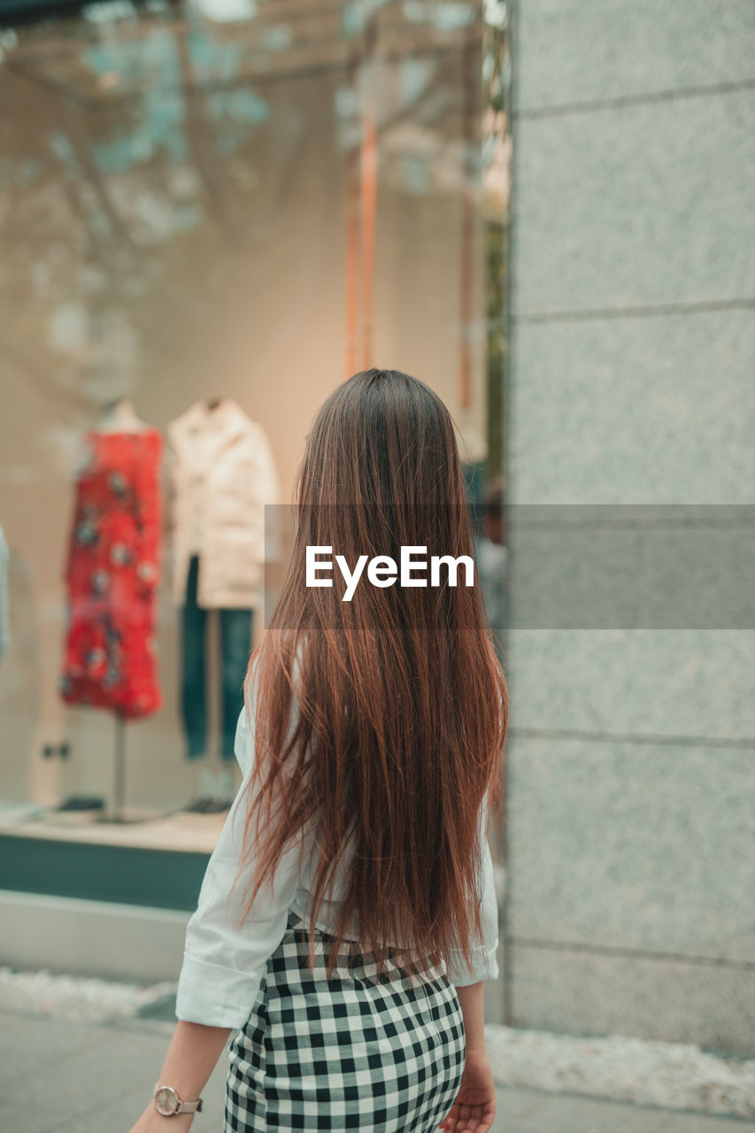 Side view of woman standing on footpath by store window