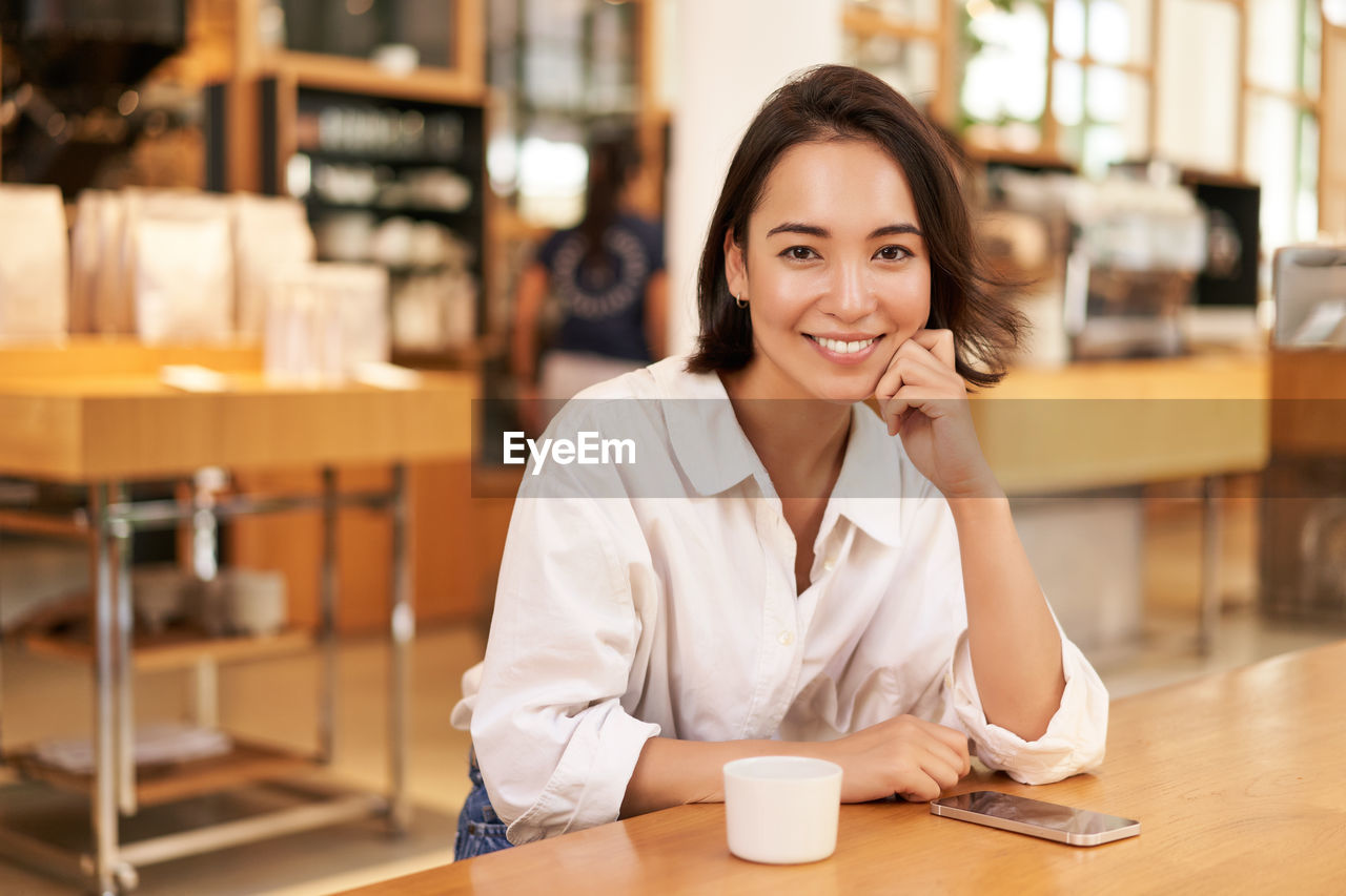 young woman using mobile phone while sitting at cafe