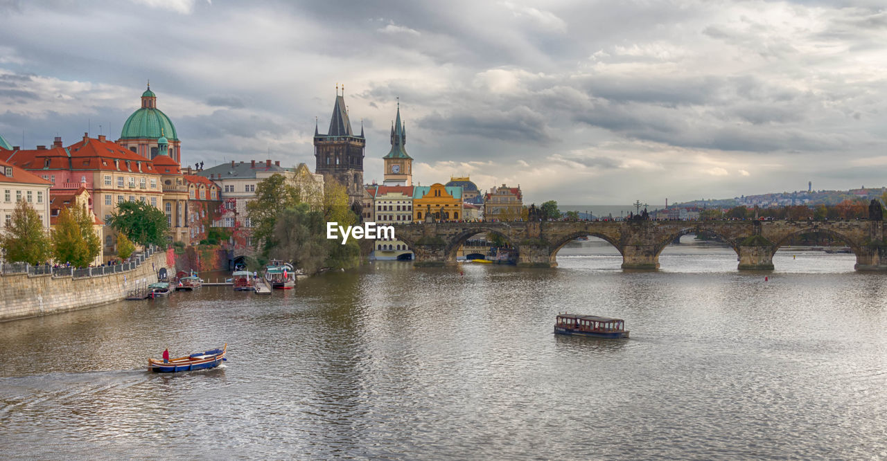 Arch bridge over river by buildings against cloudy sky in city