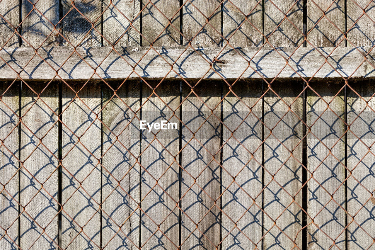The weathered old gray wooden fence is closed by a rusted netting netting.
