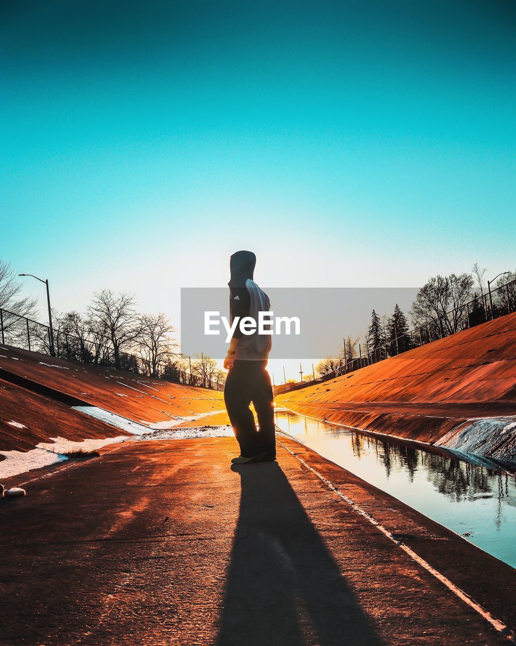 REAR VIEW OF MAN STANDING ON ROAD AGAINST SKY