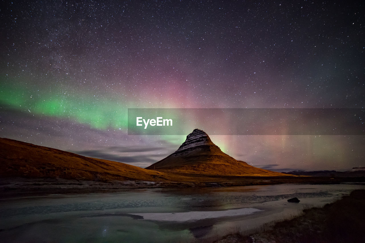 Scenic view of sea by mountain against sky at night