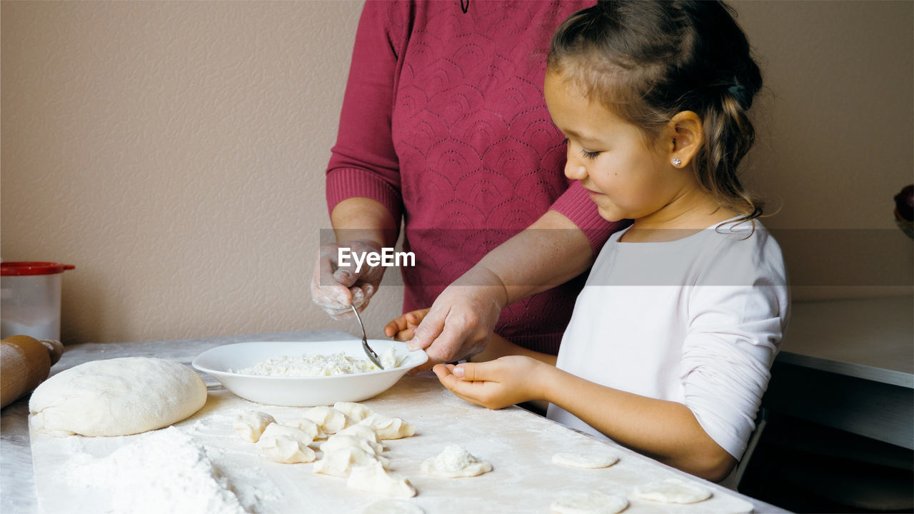 Midsection of mother with daughter preparing food on table at home