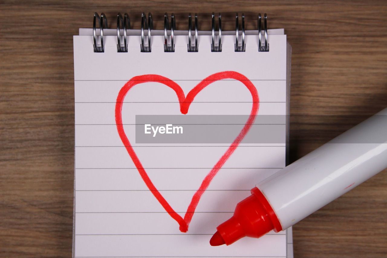 High angle view of heart shape on note pad over wooden table