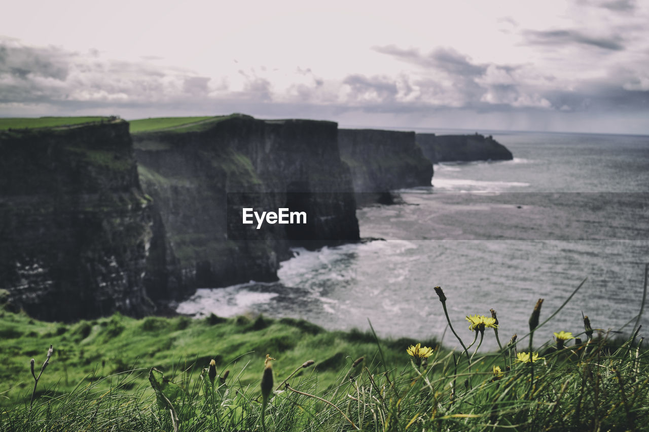 Scenic view of sea by cliff against sky during sunset