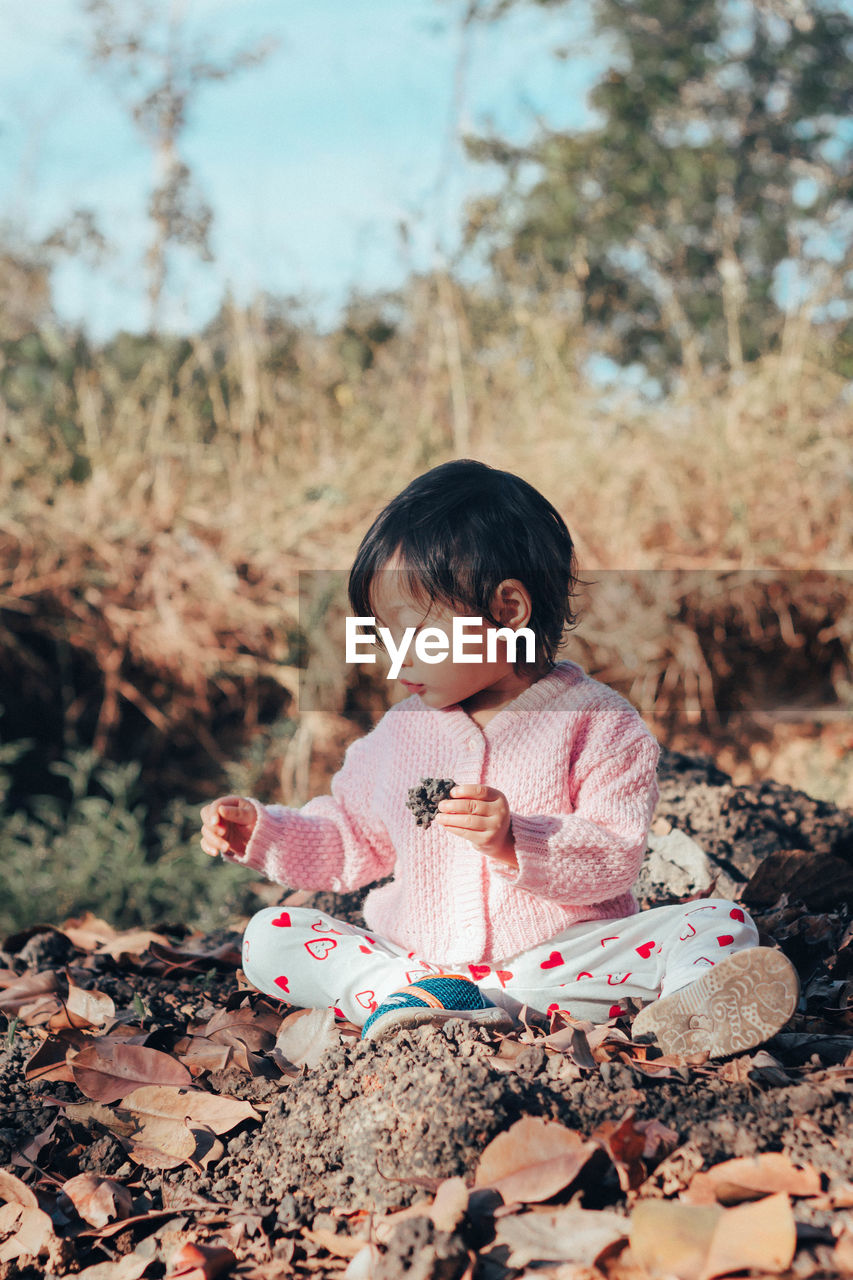 Cute baby girl looking at stone while sitting on land