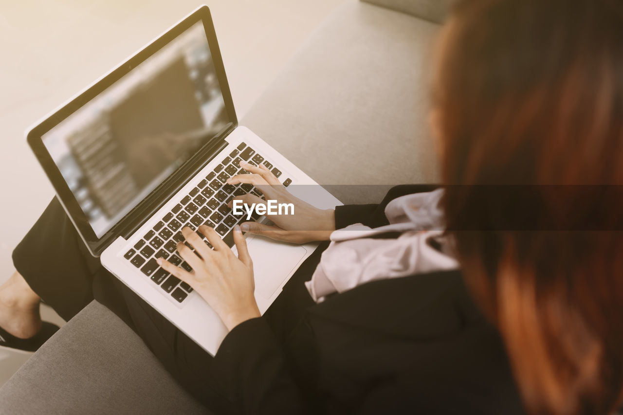 REAR VIEW OF WOMAN USING PHONE AT HOME