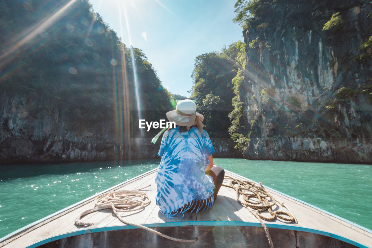 Rear view of woman sitting on boat in sea against rock formations