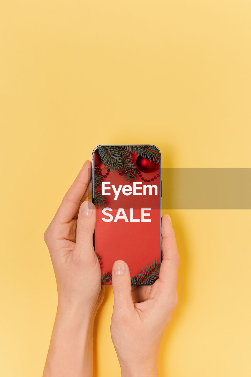 cropped hands of woman holding mobile phone against yellow background