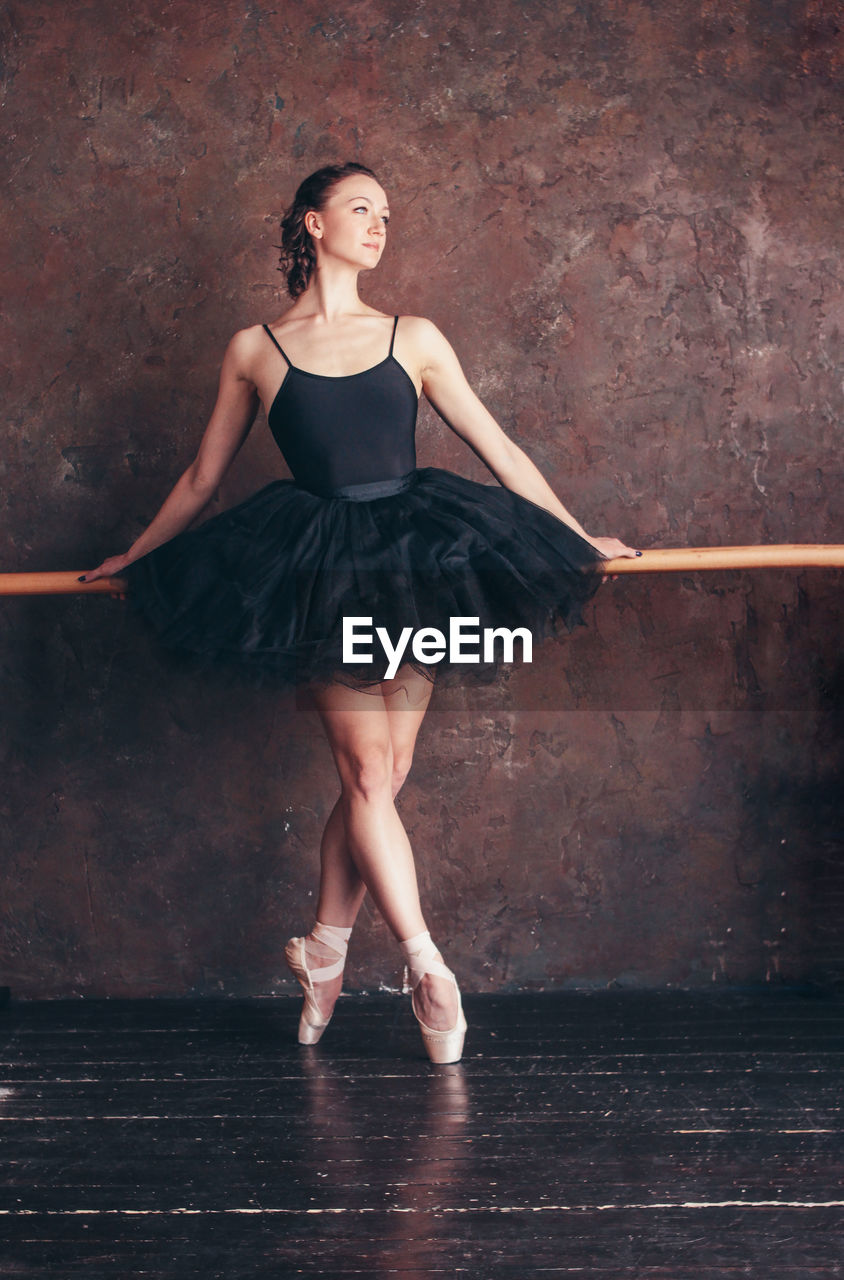 Full length of young woman dancing against wall in dance studio