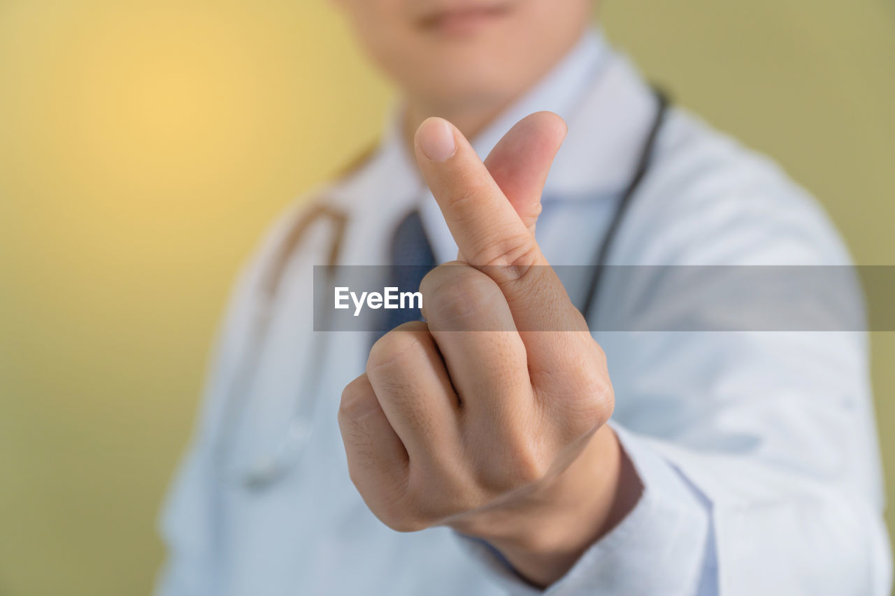 Midsection of male doctor gesturing against yellow background