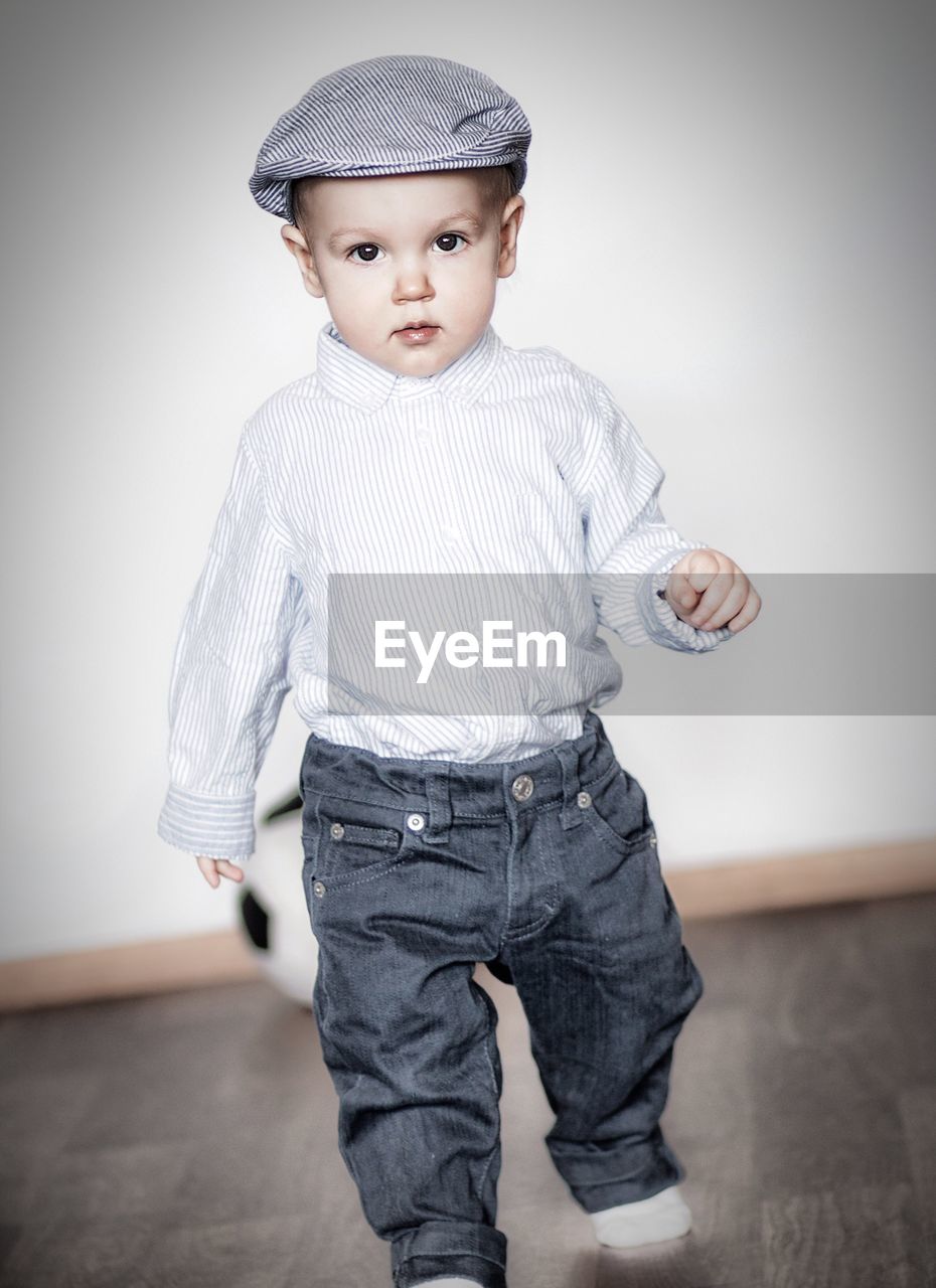 Portrait of boy wearing flat cap walking against wall at home