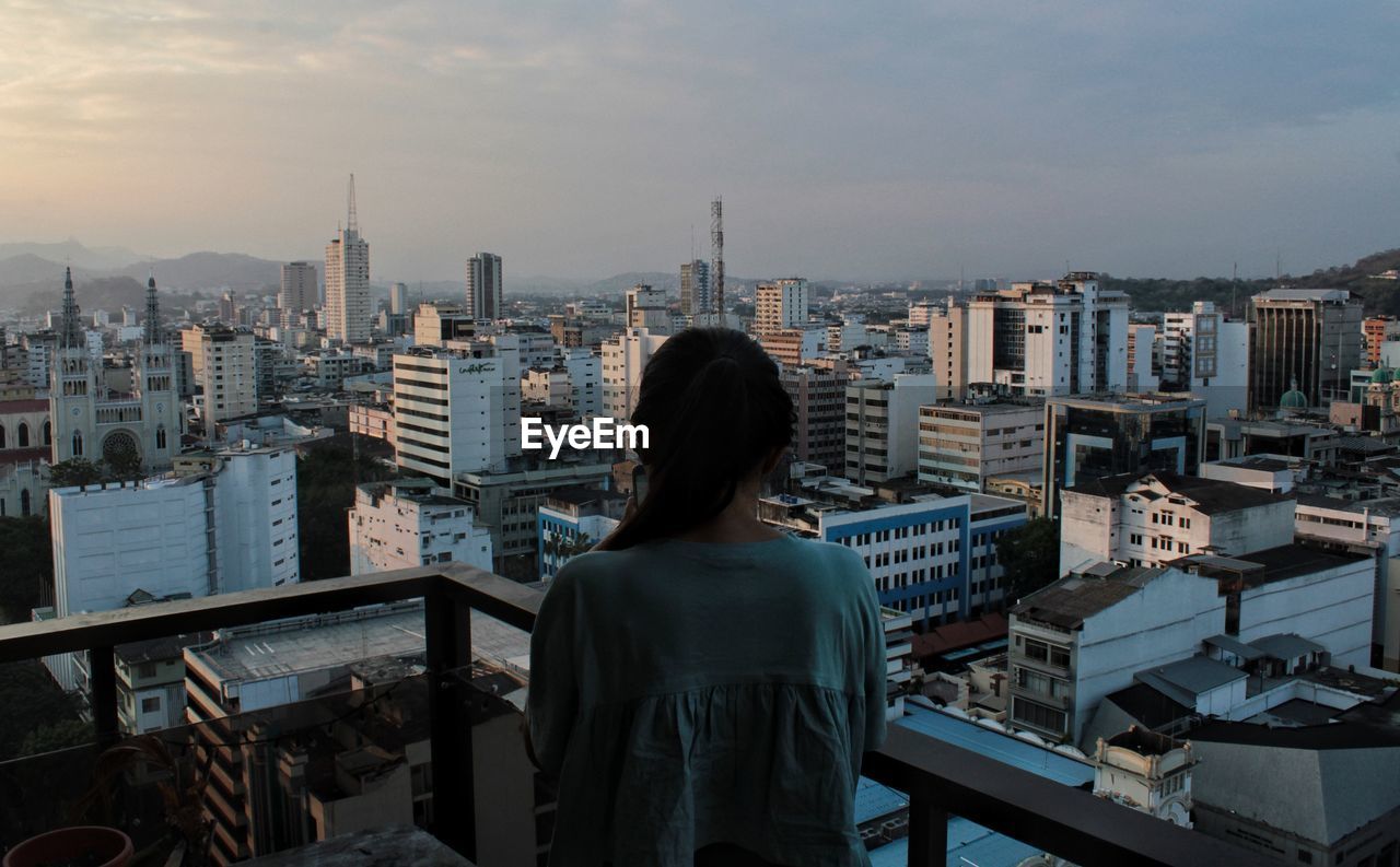 Rear view of woman standing at balcony against cityscape