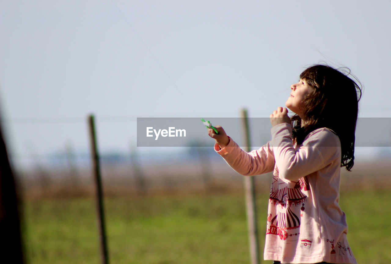 Side view of cute girl holding toy while standing on field