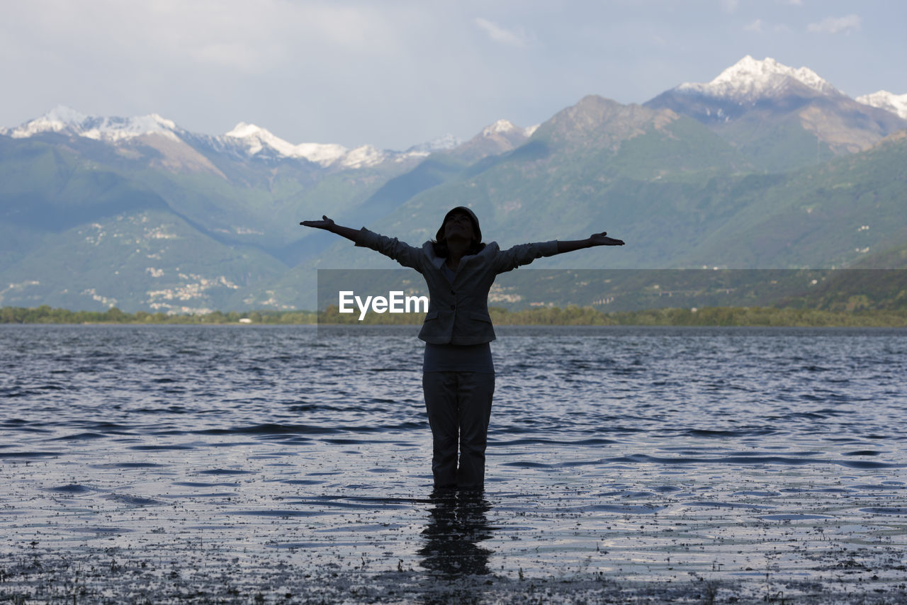 Woman standing with arms outstretched in lake maggiore against mountains