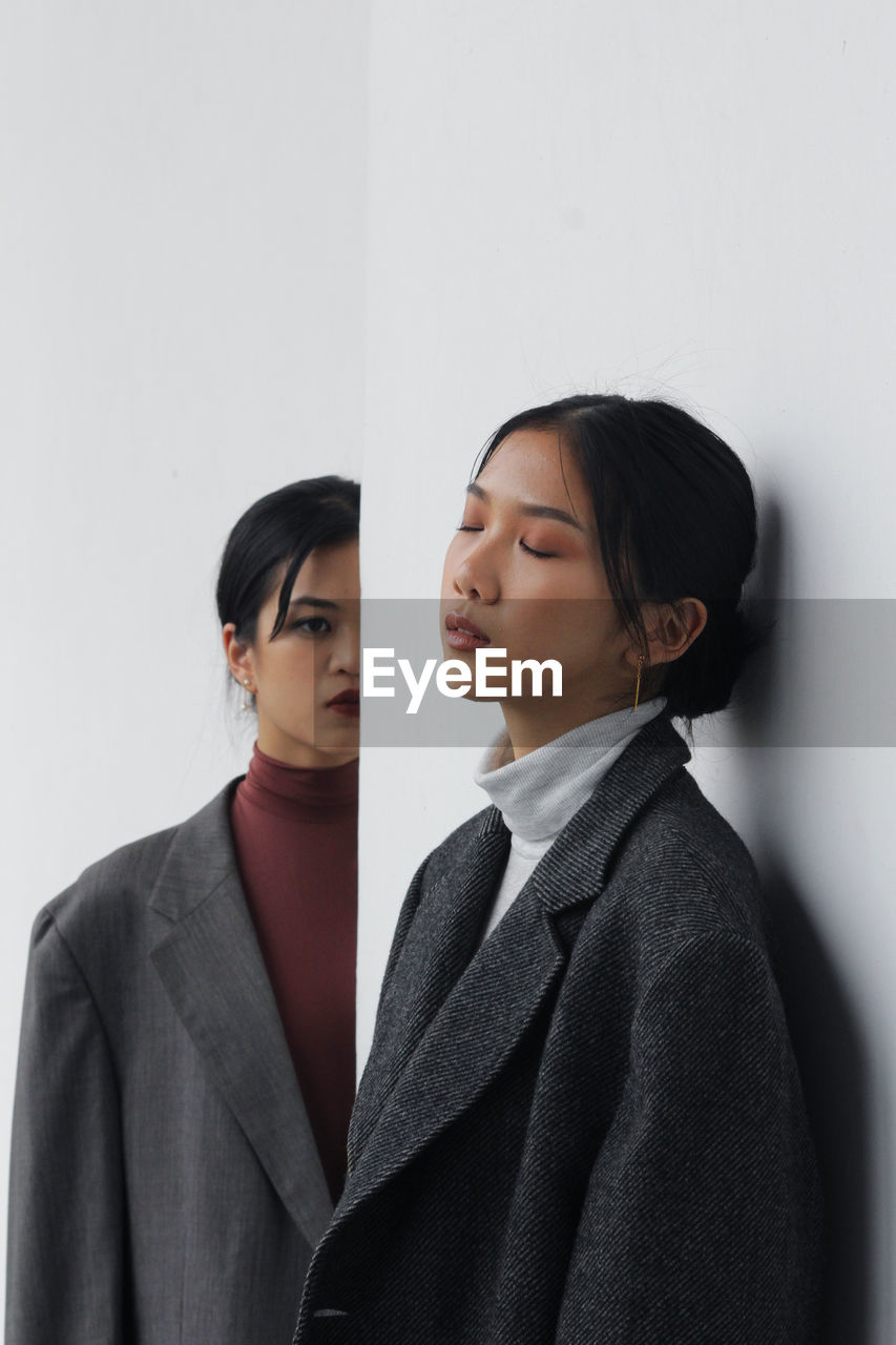 Young woman looking at friend with eyes closed standing against wall