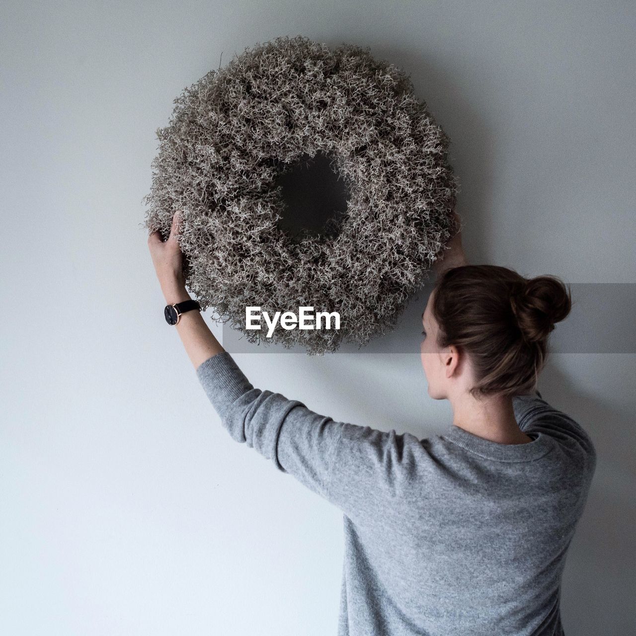 Rear view of woman placing wreath decoration on wall at home