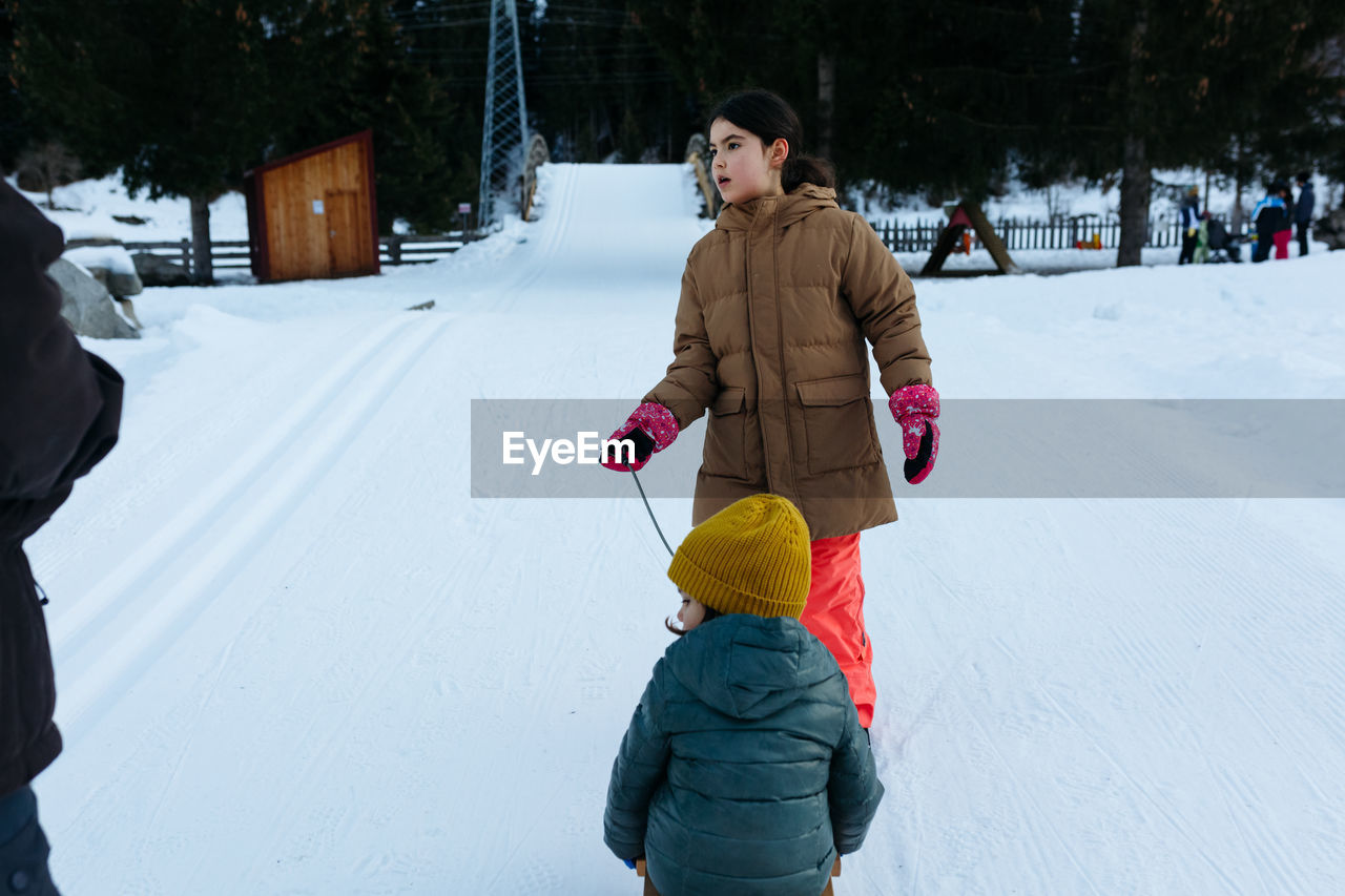 Elder sister pulling smaller sister on wooden sled