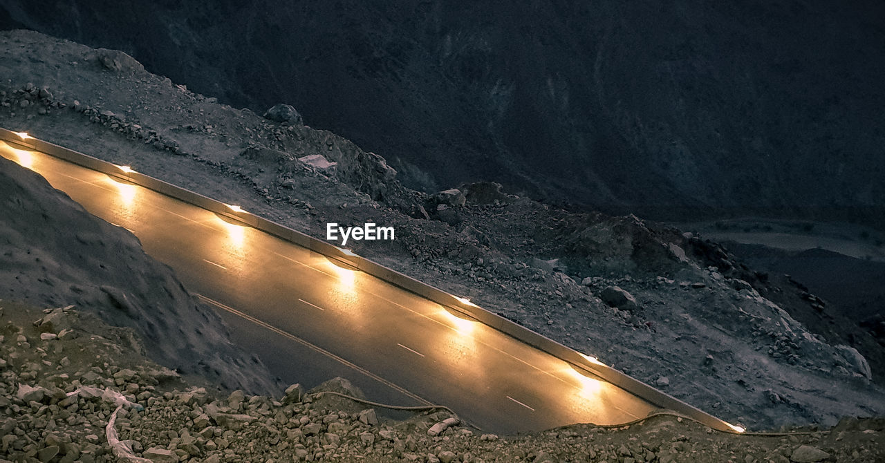 SCENIC VIEW OF ROAD BY MOUNTAIN AT NIGHT