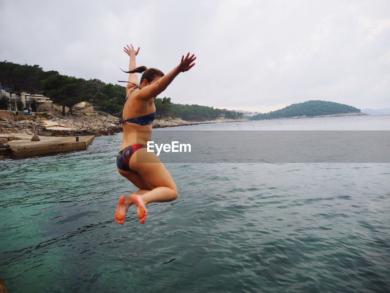 Full length of young woman wearing bikini diving in sea against sky