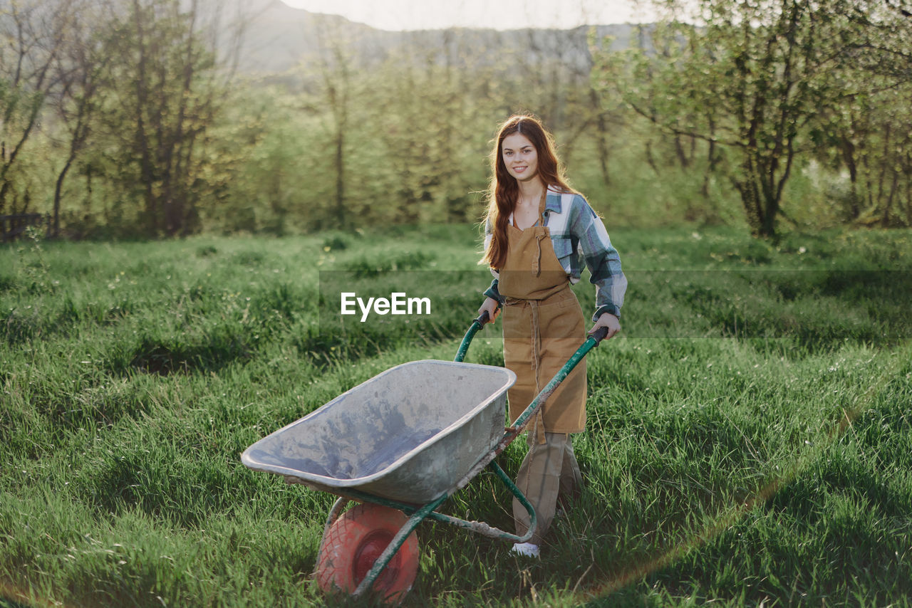 Portrait of young female farmer walking with wheelbarrow on field