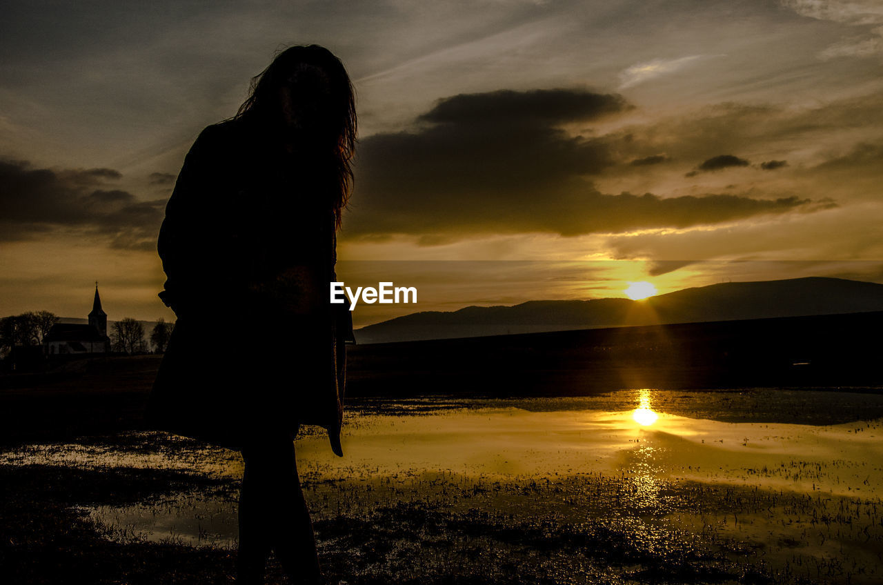 Woman walking at beach against sky during sunset