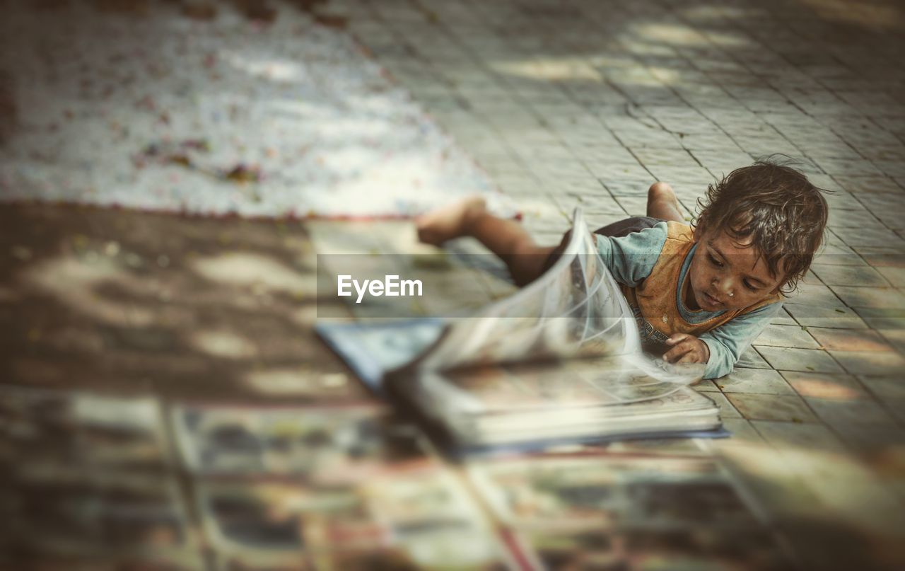 Girl looking at book while lying down on footpath