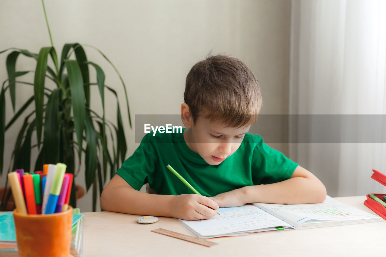 7 years old child boy doing lessons sitting at desk in his room. kid writing homework in notebook