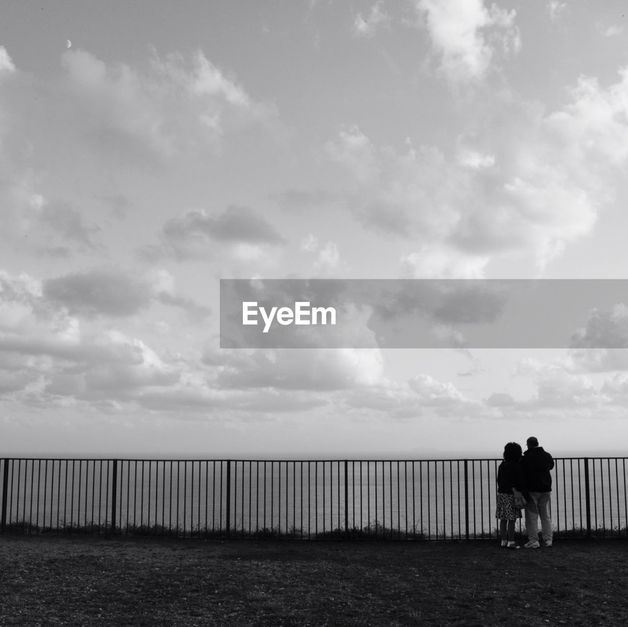 REAR VIEW OF COUPLE STANDING ON RAILING AGAINST SEA