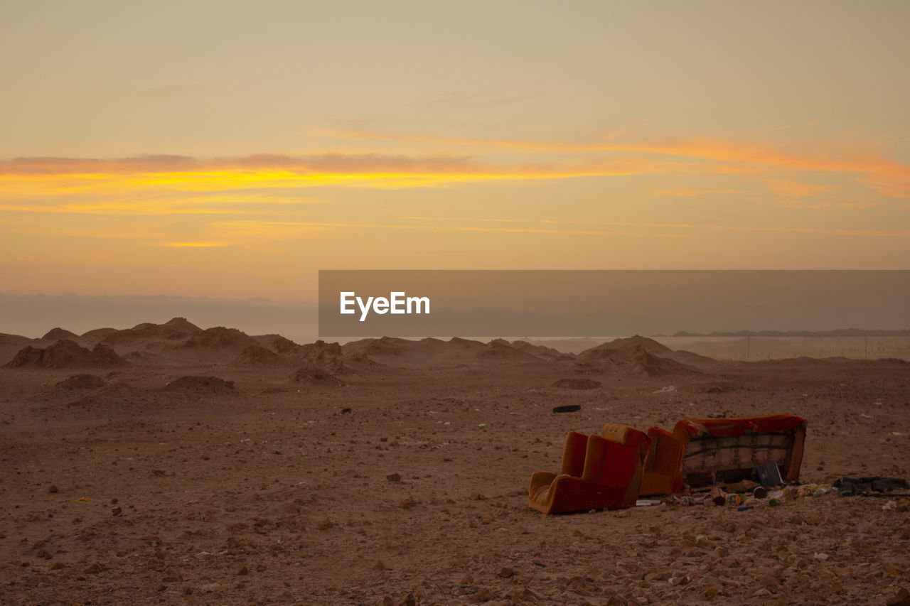 Vintage sofa throwed into garbage in the middle of the desert during golden sunset