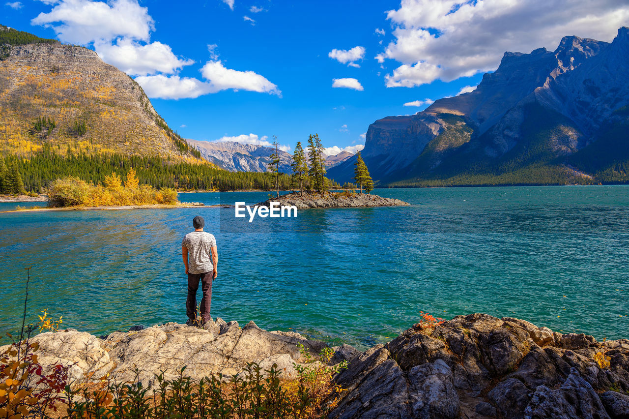 rear view of woman walking on rock by lake against sky