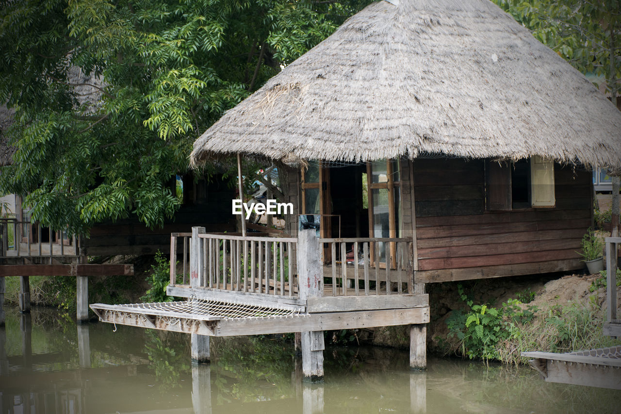 Wooden house beside the water, thatched with grass, with trees beside, sitting beside the river