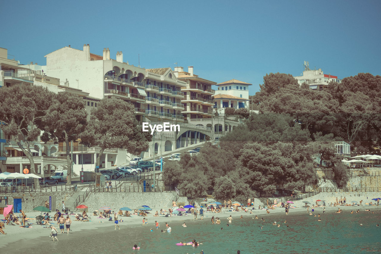 Group of people on beach in porto cristo against townscape and blue sky