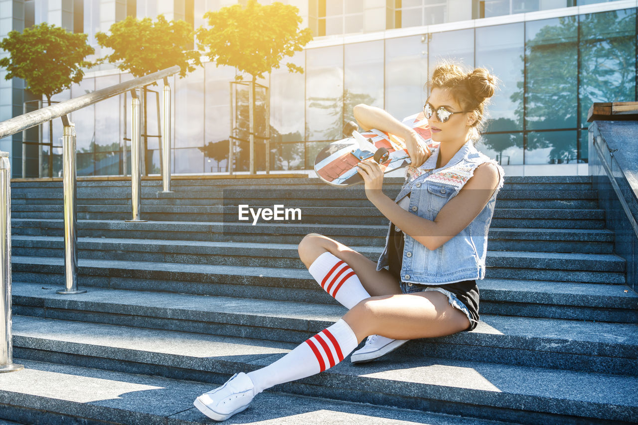 Full length of woman with skateboard sitting on steps outdoors