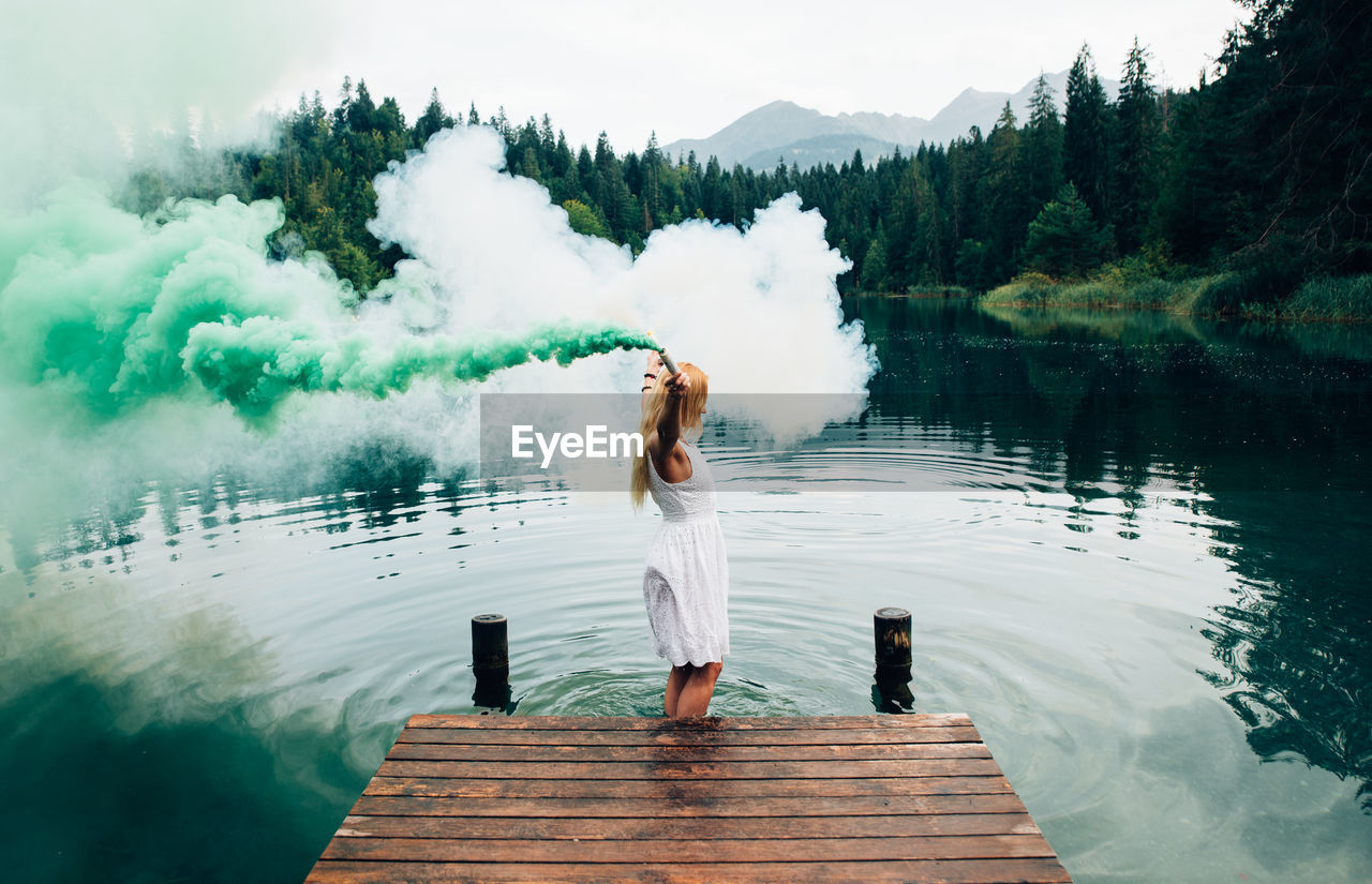 REAR VIEW OF WOMAN STANDING ON PIER IN LAKE