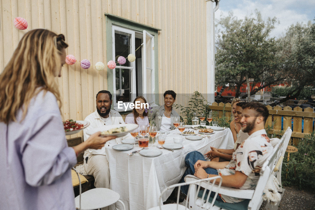 Woman serving food to male and female friends during dinner party at cafe