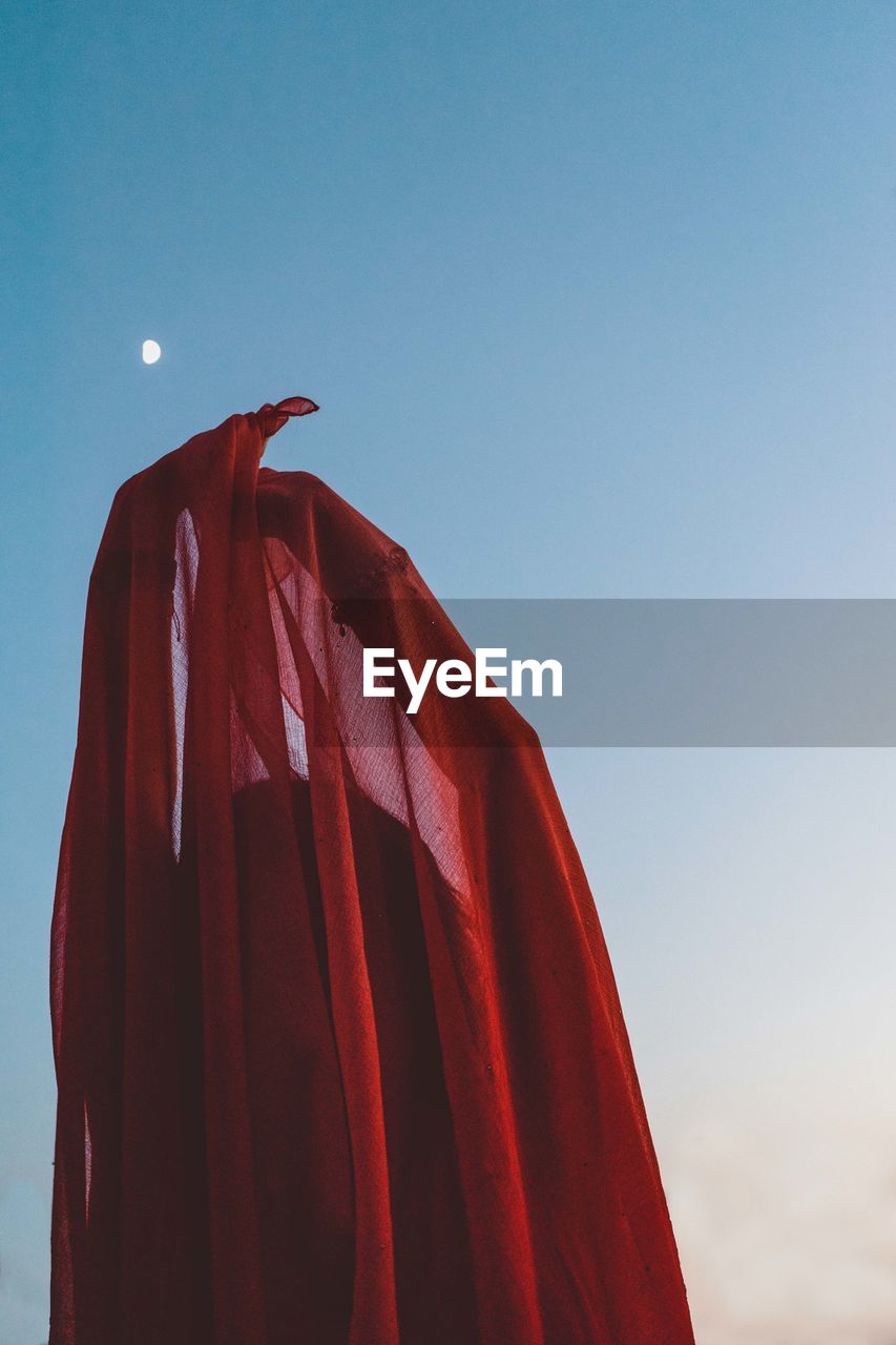 Model covering her face with fabric and the moon is visible in the background.