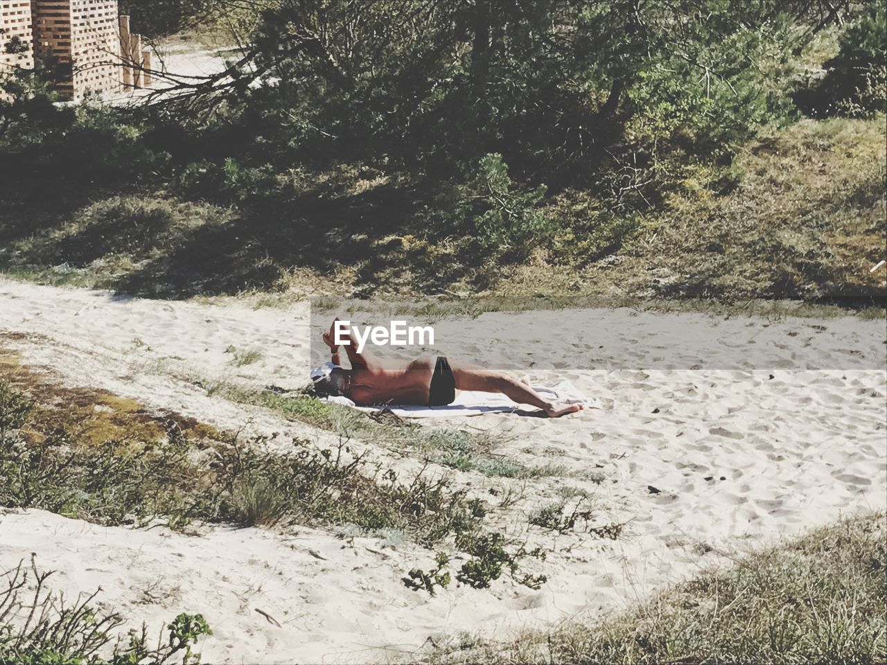 Shirtless man lying on sand during sunny day