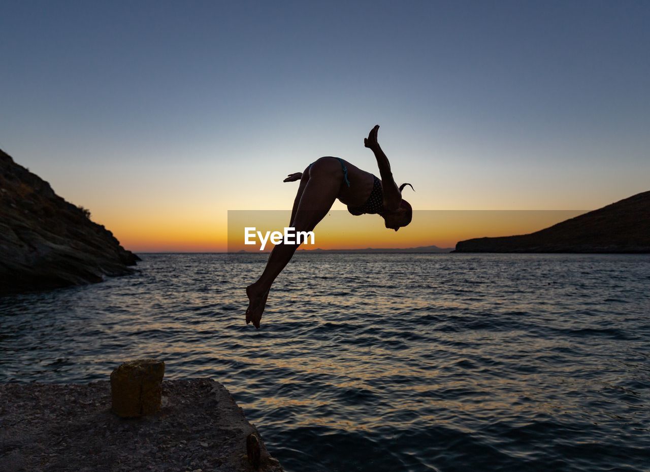 SILHOUETTE OF JUMPING IN SEA AGAINST CLEAR SKY