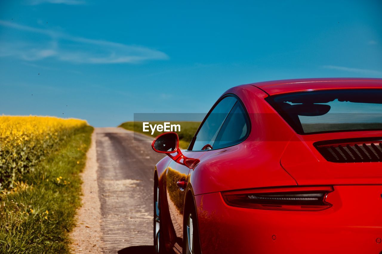 Red car on road against blue sky during sunny day