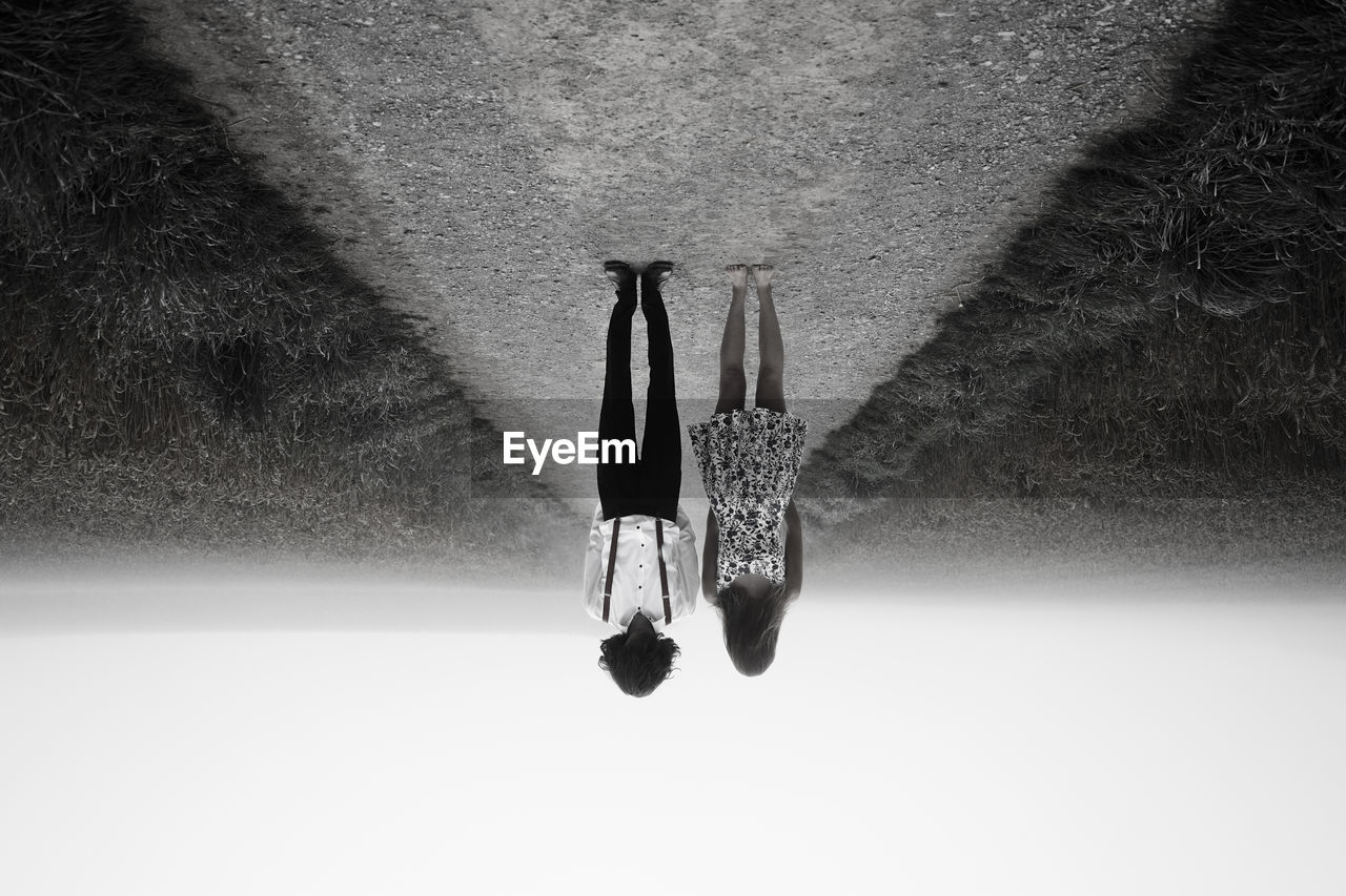 Upside down image of man and woman standing on road amidst field