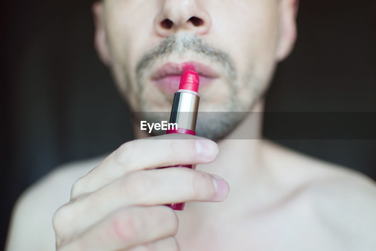 Midsection of transgender man applying red lipstick
