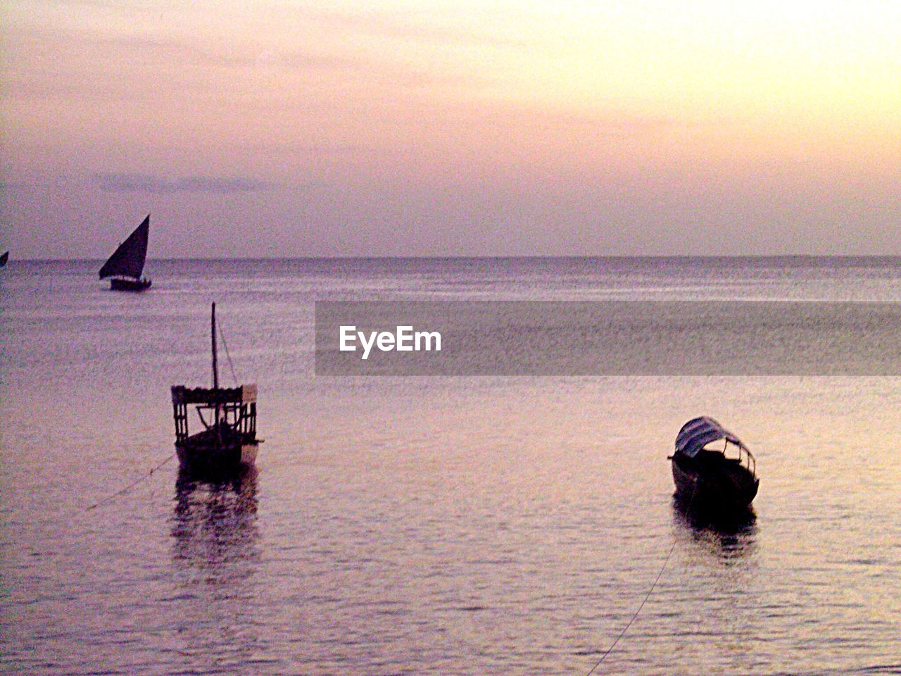 BOATS SAILING IN SEA AT SUNSET