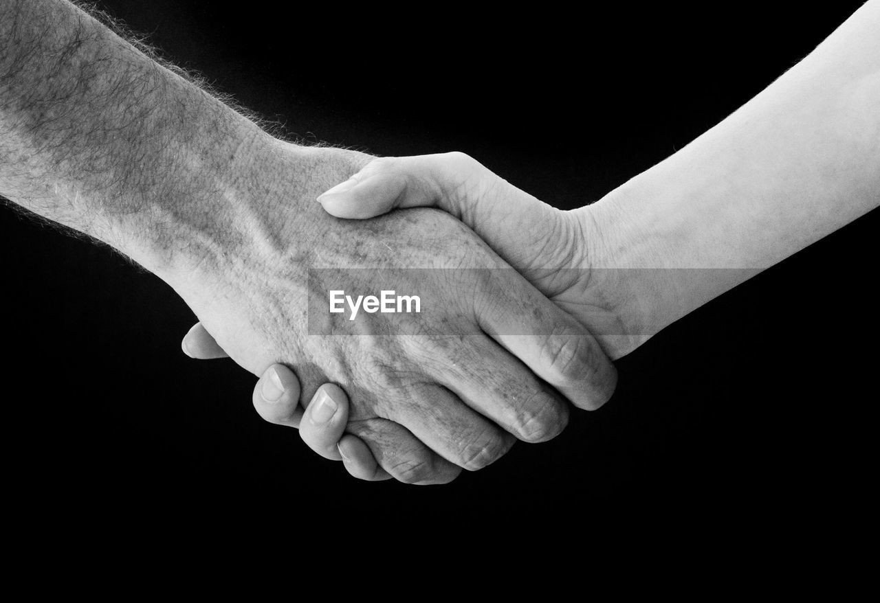 Cropped image of people doing handshake against black background