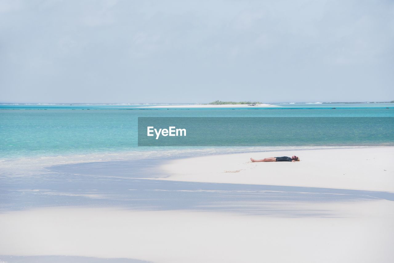 Mid adult woman relaxing on sand at beach against sky