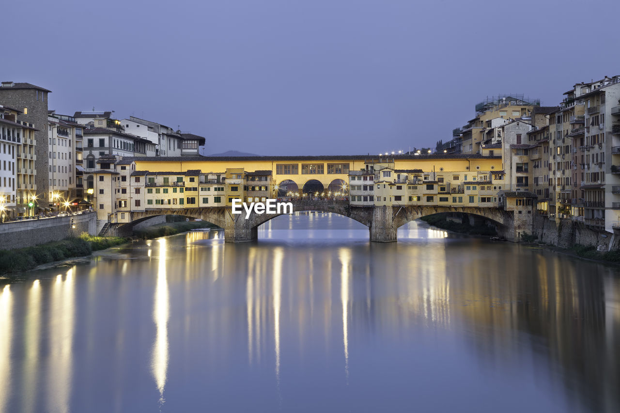 Illuminated ponte vecchio over arno river in city at dusk