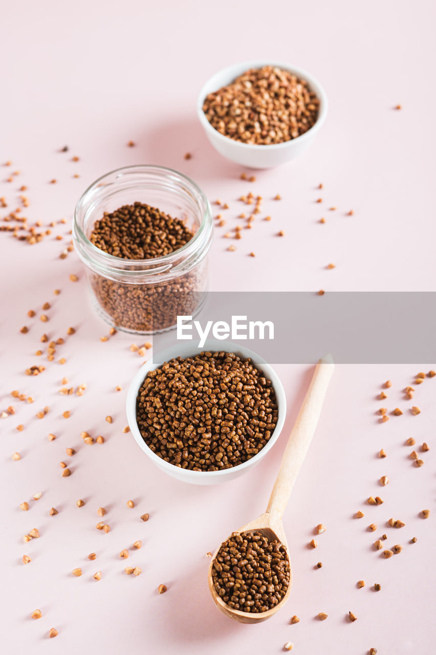 Raw buckwheat tea in a bowl and wooden spoon and buckwheat on the table vertical view