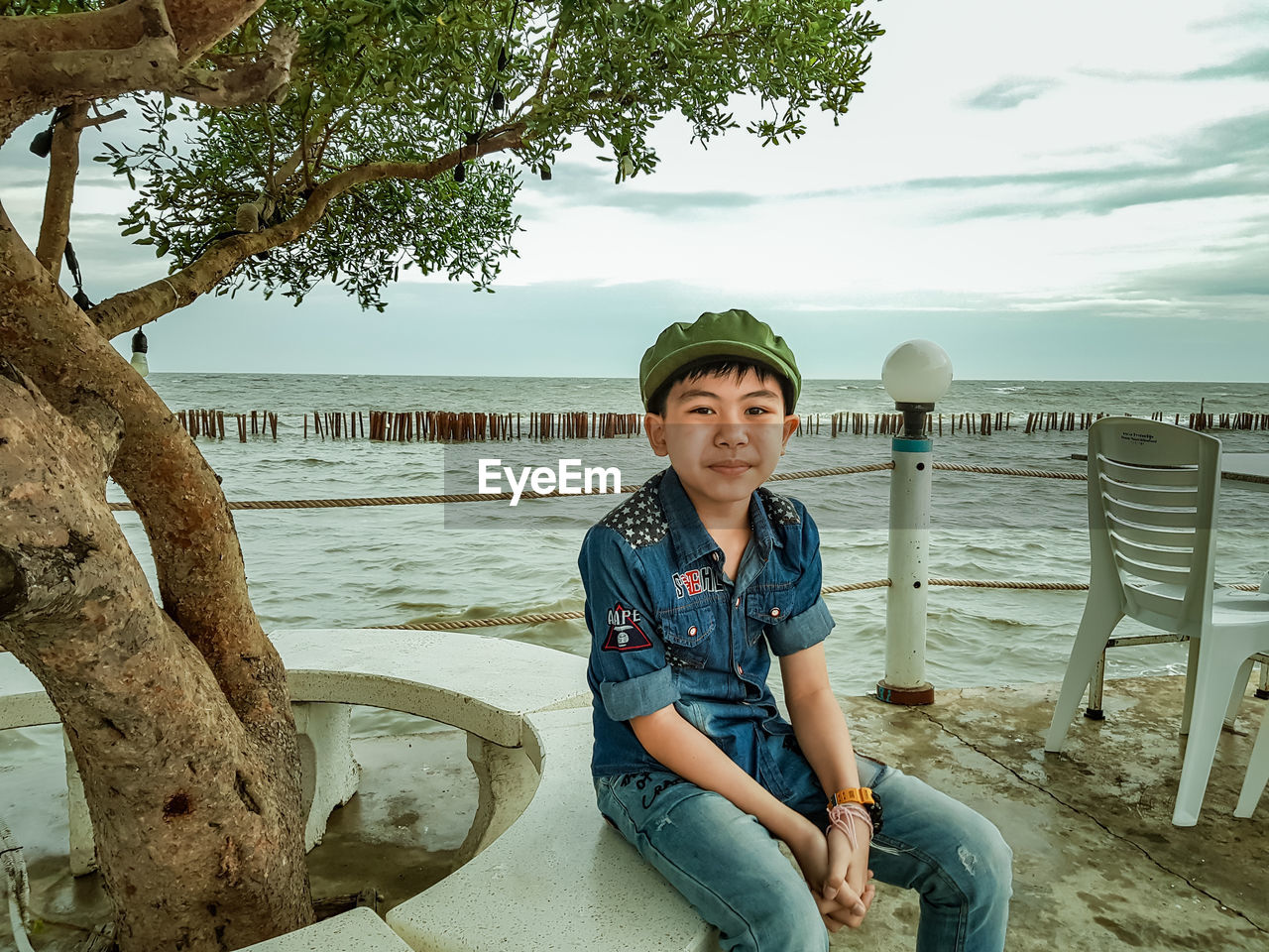 Portrait of boy sitting by tree against sea and sky