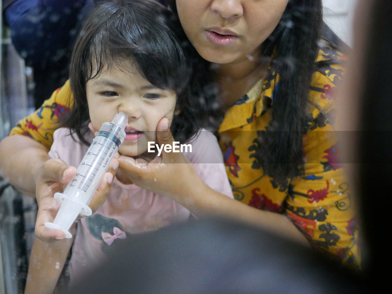 Asian mom rinsing her baby's stuffy nose using a syringe of saline water