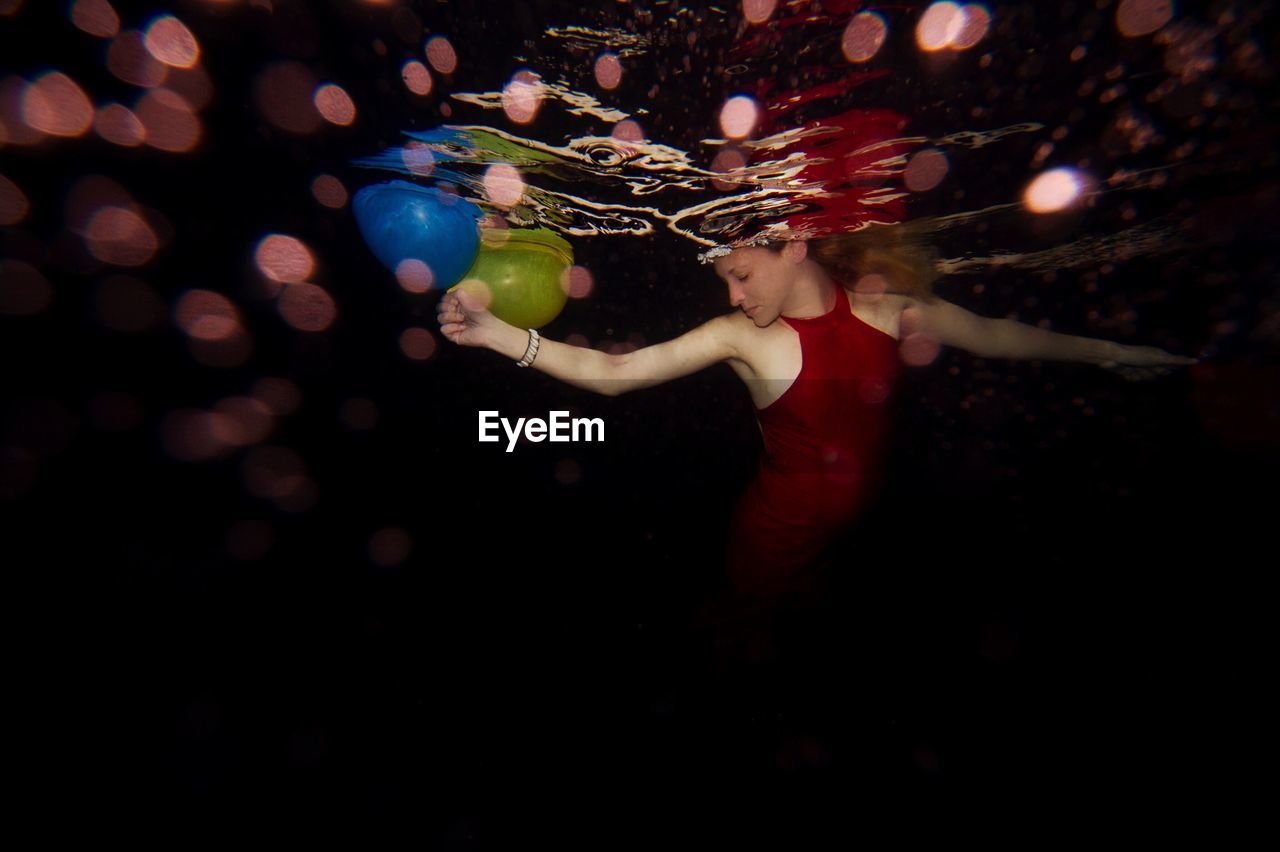 Woman swimming in pool with balls at night